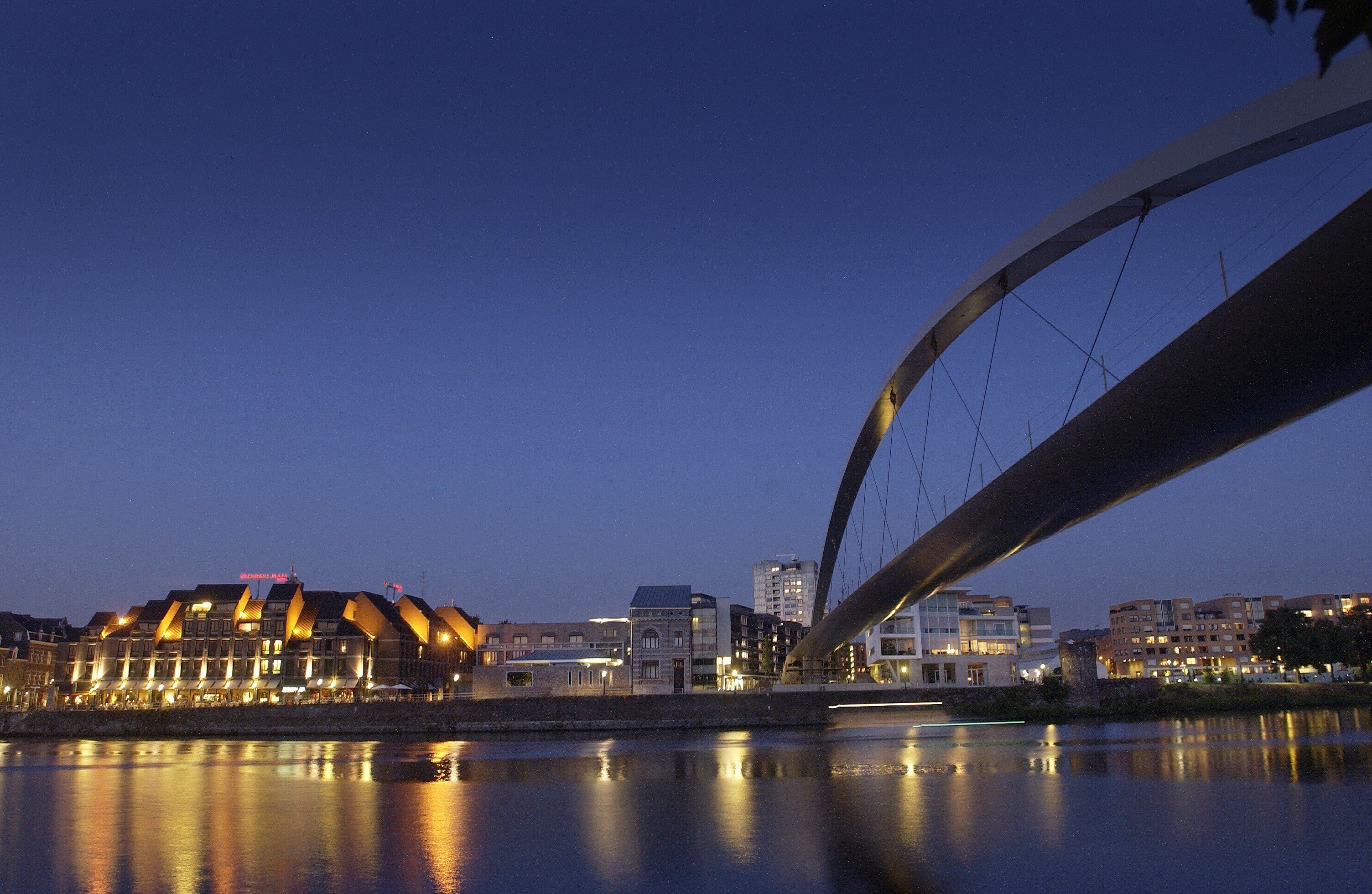 A waterfront view with a modern bridge, buildings with illuminated signs, and a calm river reflecting the lights.