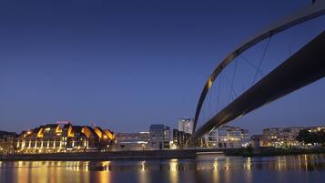 A waterfront view with a modern bridge, buildings with illuminated signs, and a calm river reflecting the lights.