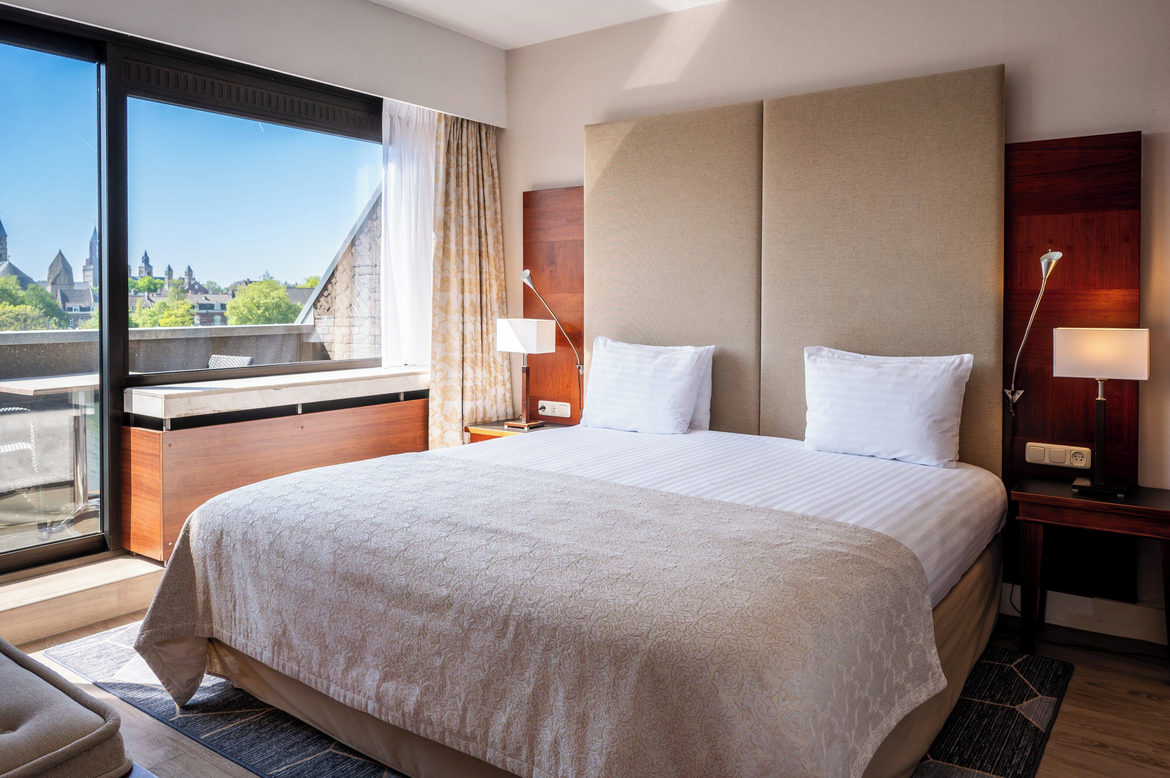 A hotel room with a large bed, a desk, and a window with a view of buildings.