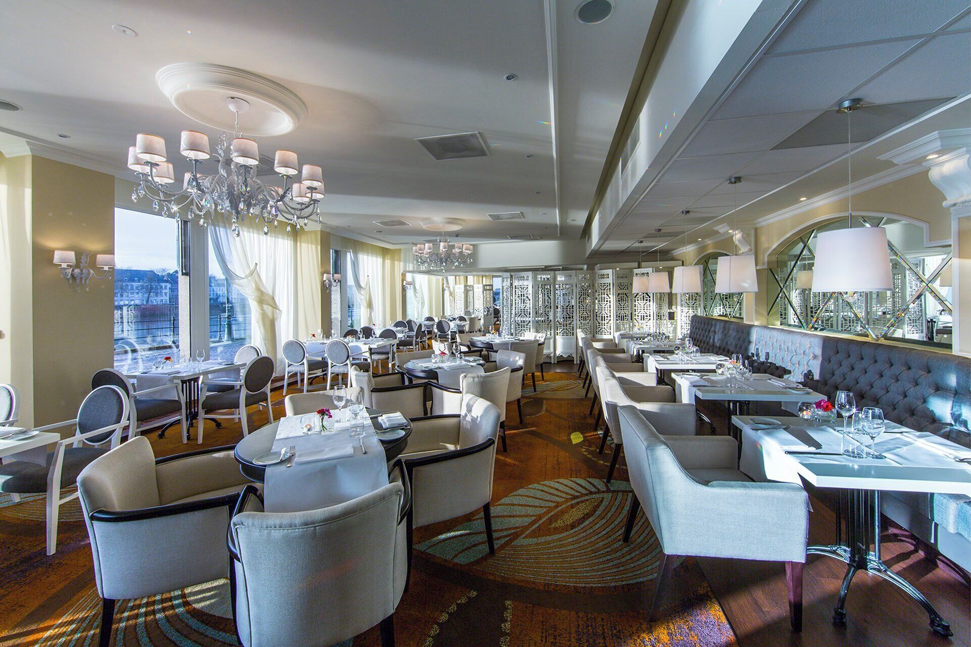 Een restaurantgedeelte in een hotel met meerdere tafels en stoelen, kroonluchters en grote ramen met uitzicht.