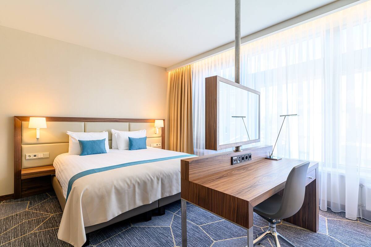 Een hotelkamer met een bed, bureau, stoel en grote ramen.