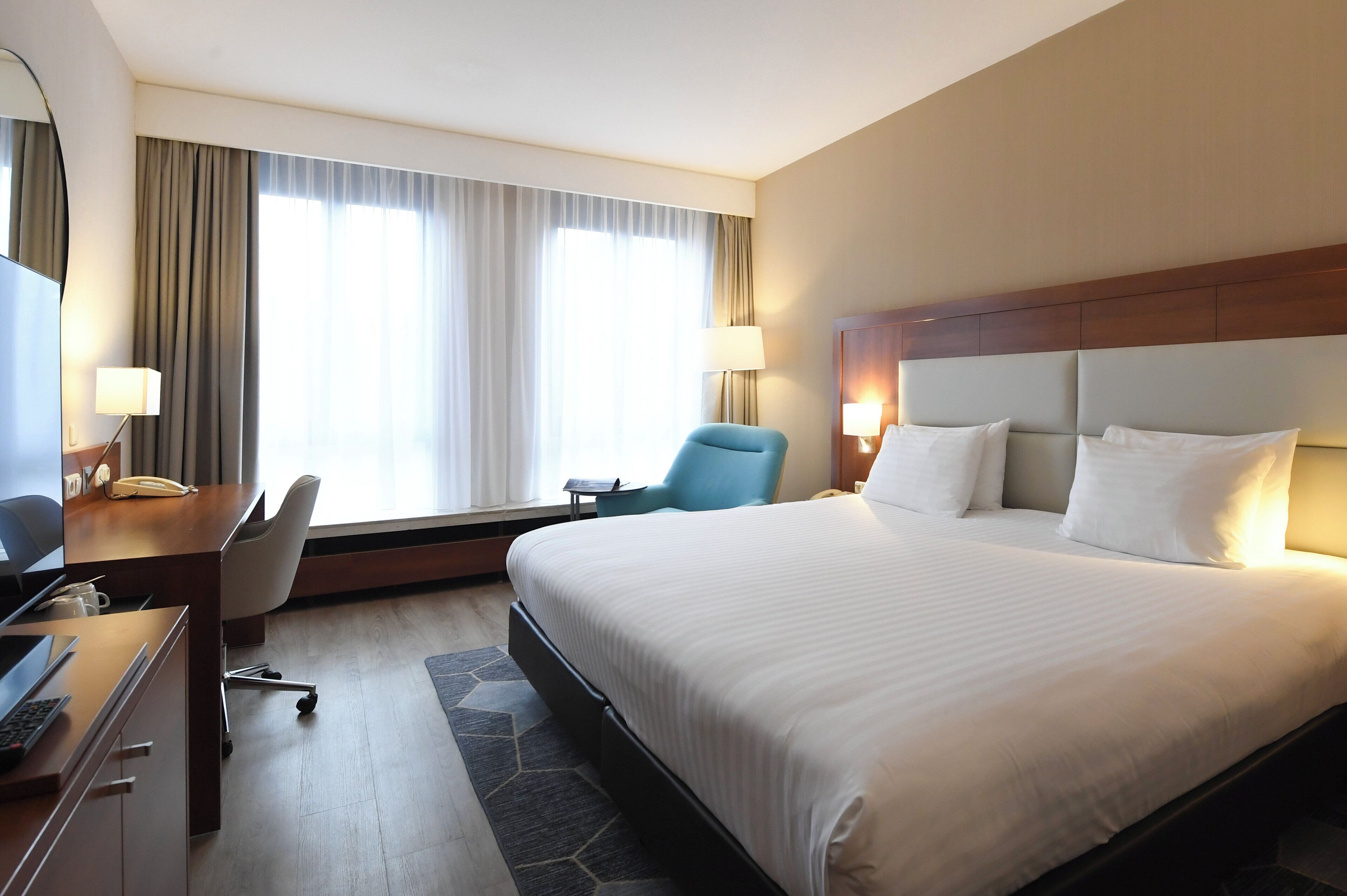 Een hotelkamer met een groot bed, een bureau met een computer, een stoel en een raam met gordijnen.