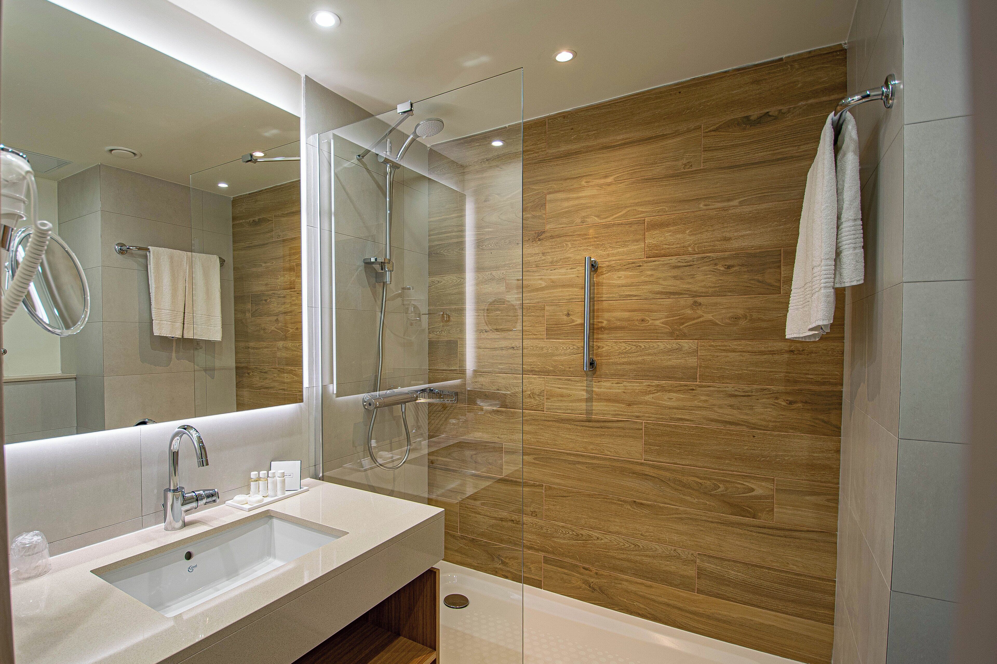 A modern bathroom with a large mirror, a sink, a shower with a glass enclosure, and wooden wall panels.
