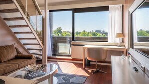 Un salon moderne avec un canapé, une table basse en verre, un bureau et une vue sur le paysage urbain, visible à travers de grandes fenêtres.