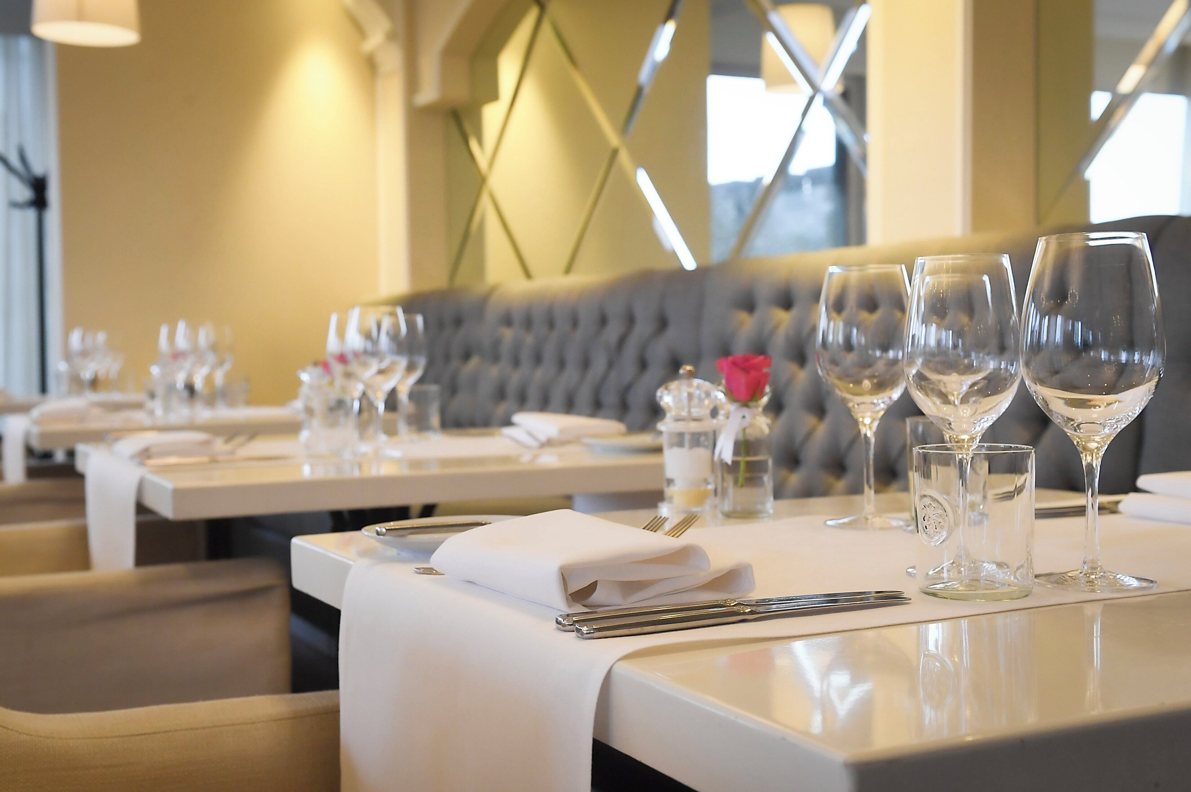 L’intérieur d’un restaurant, avec des tables disposées de manière ordonnée, chacune agrémentée de verres à vin, de couverts et de serviettes pliées.