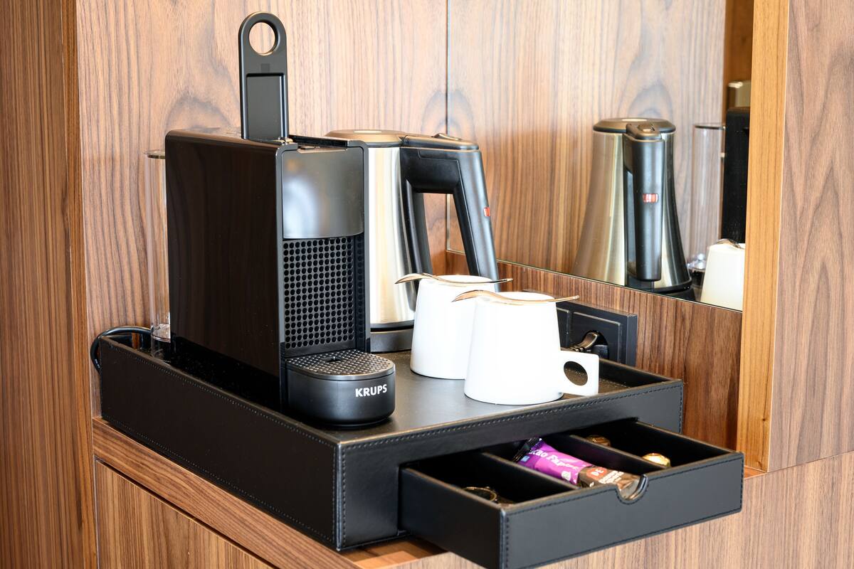 A coffee maker, a cup, and a drawer with a pen and a small item.