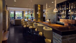 Een bar met een accentmuur van steen, meerdere hangende lampen en een goed gevulde bar.