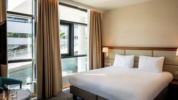 Habitación de hotel con una cama grande, vistas a un balcón y un área de descanso con mesa y sillas.
