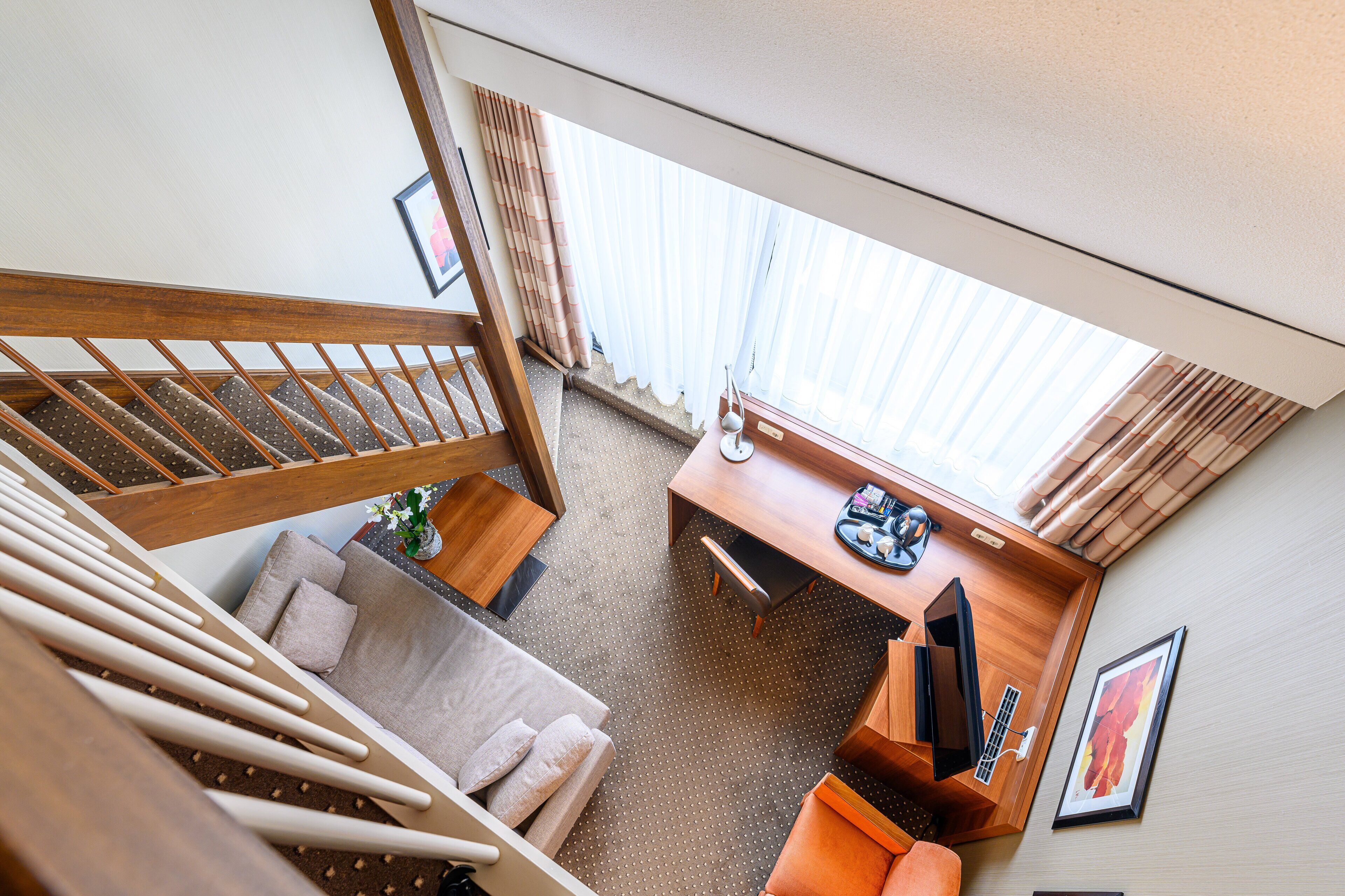 A hotel room with a staircase, a sofa, a desk, and a window with curtains.