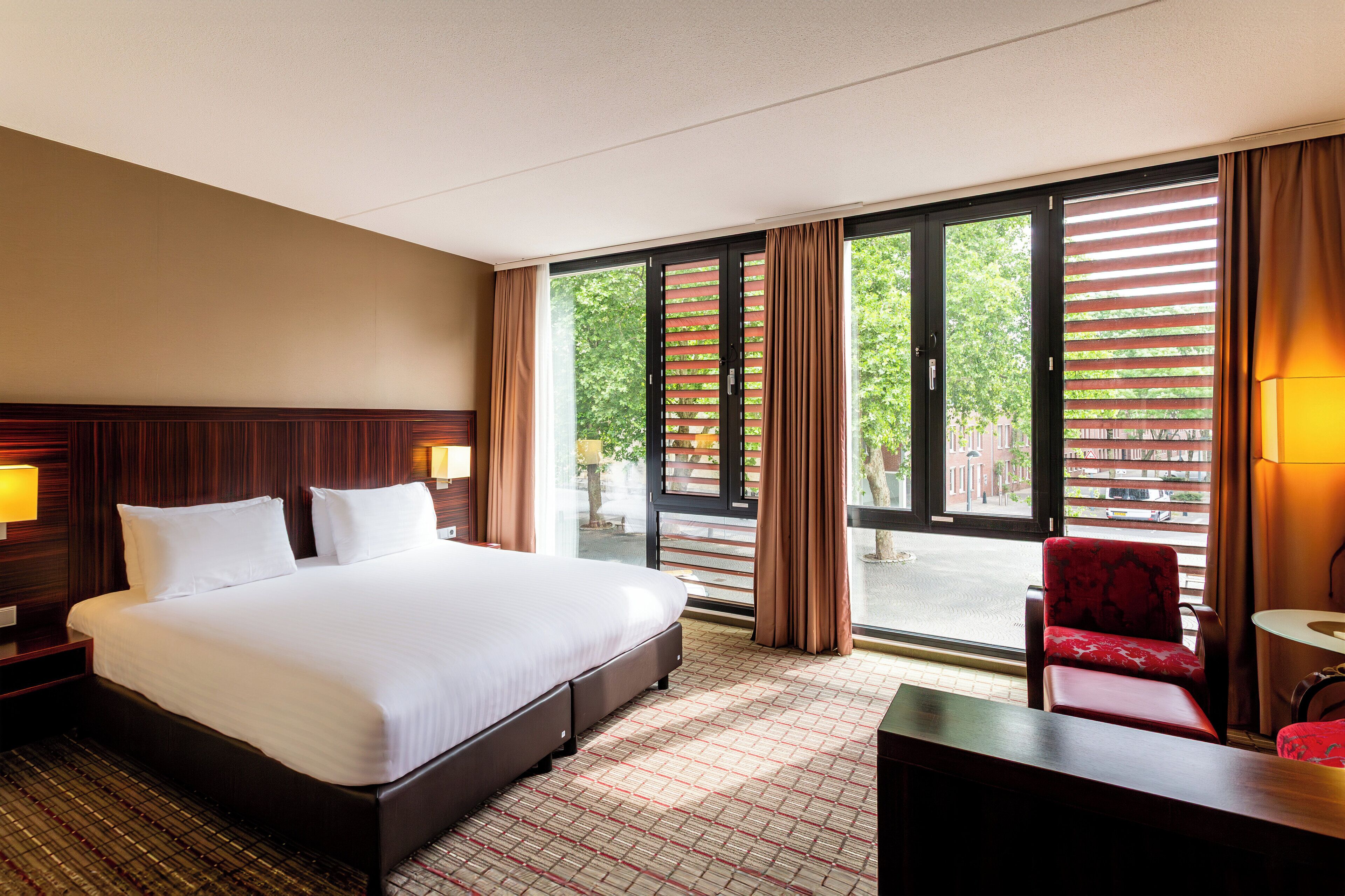 Habitación de hotel con una cama grande, un escritorio, una silla y una ventana con persianas.