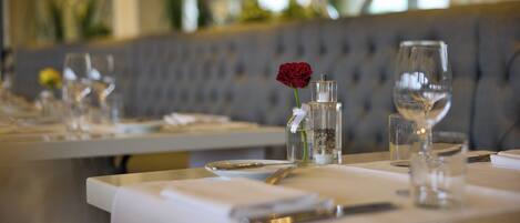 Una mesa de comedor dispuesta con un vaso de agua, una copa de vino, una rosa y un pequeño florero con una vela.