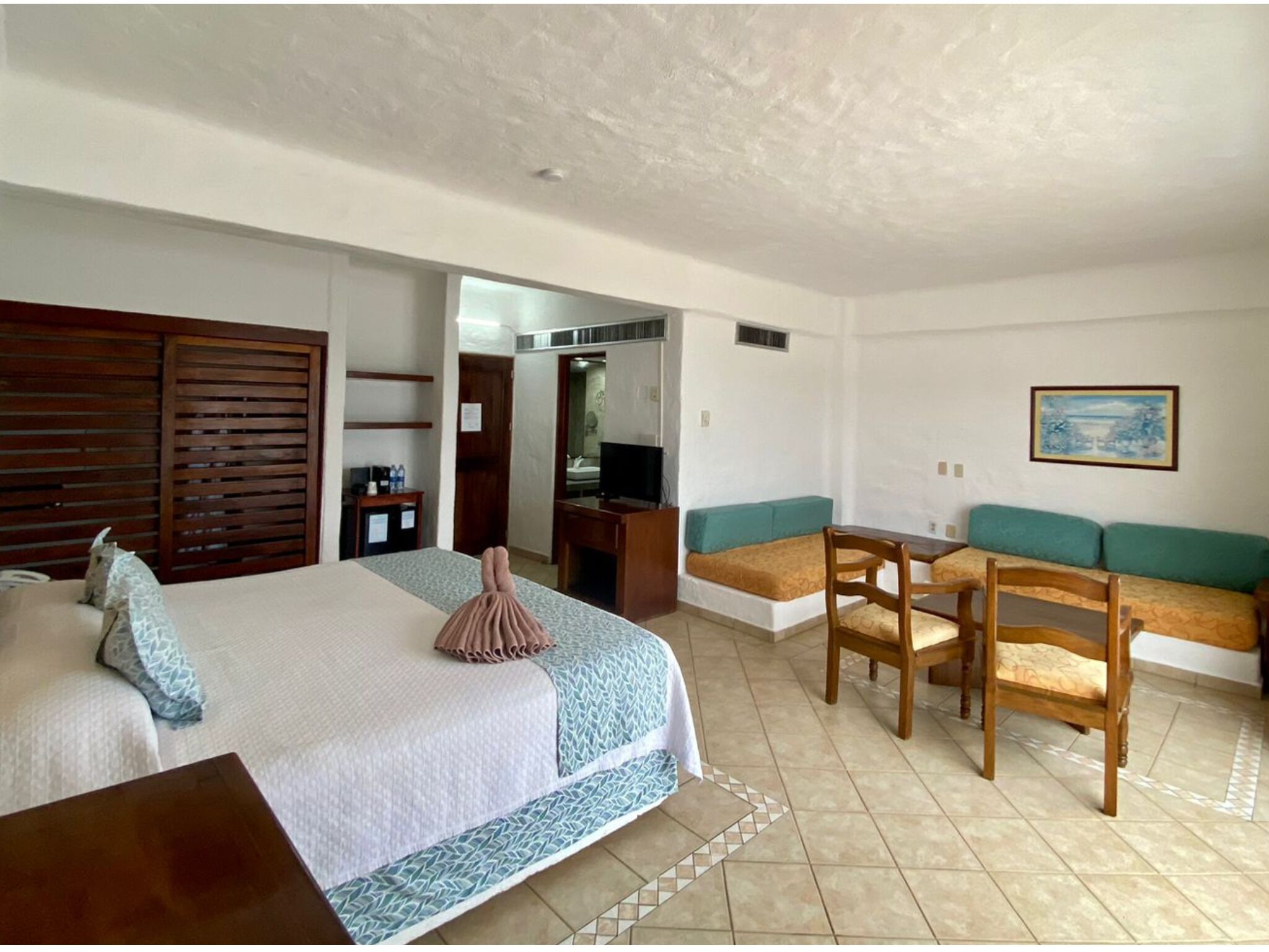 Een hotelkamer met een bed, een bureau, een stoel, een bank, een televisie en een schilderij aan de muur.