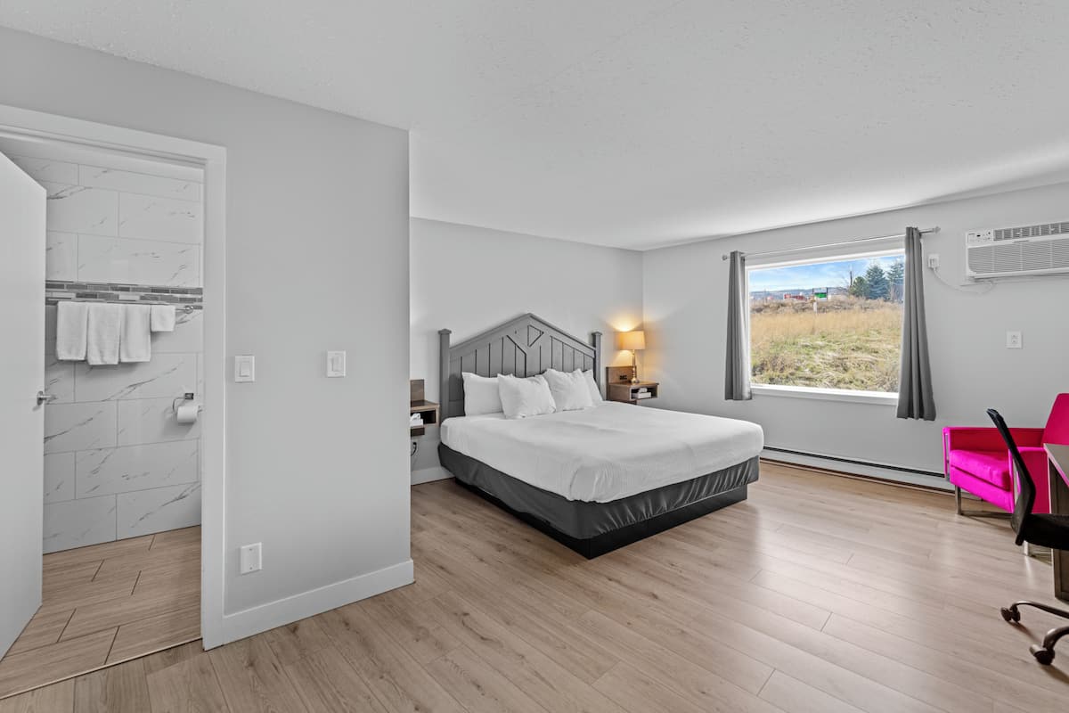 A bedroom with a bed, a nightstand, a window with curtains, a chair, and a view of the outdoors.
