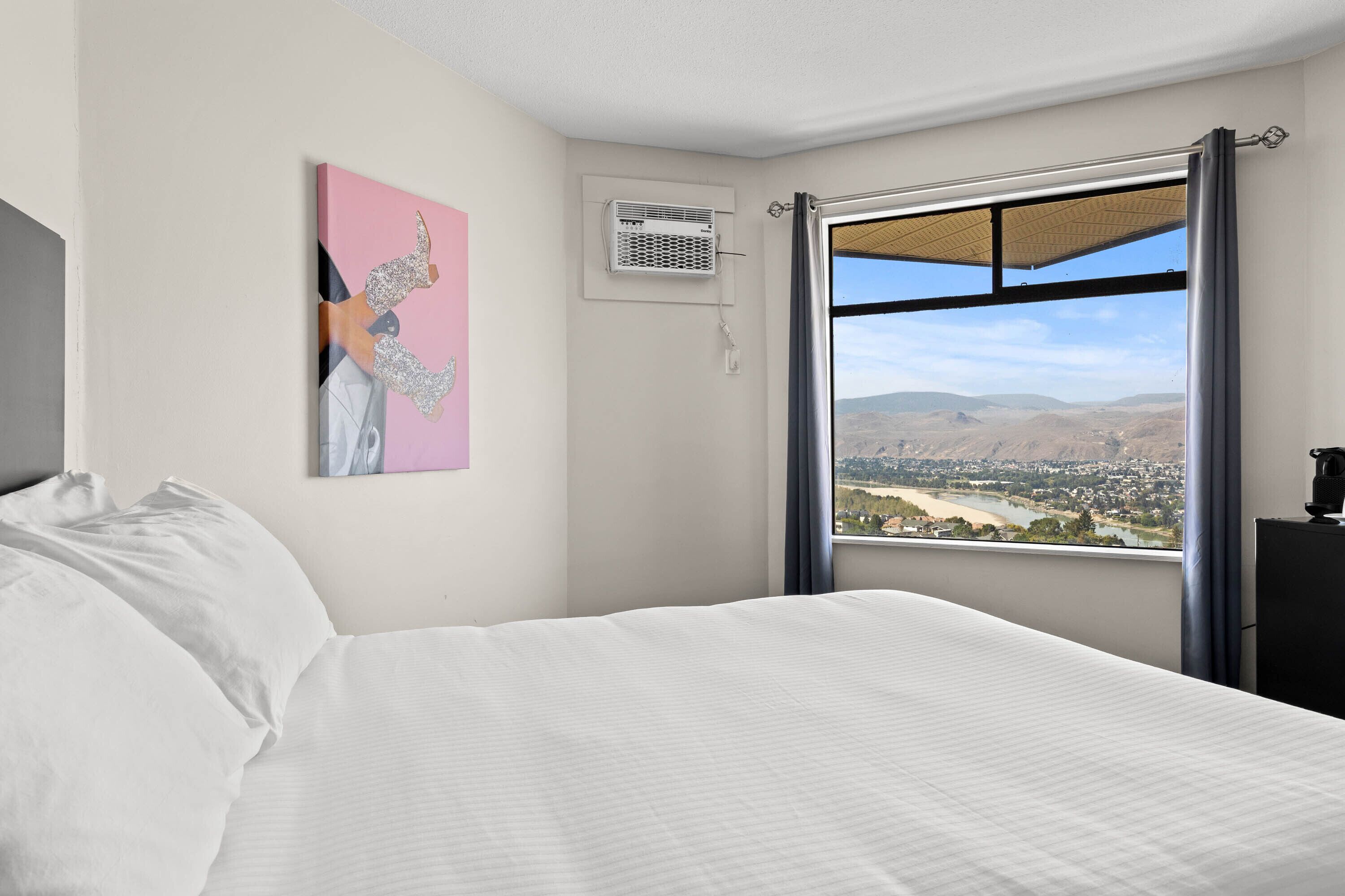 A bedroom with a bed, a window with a view of a landscape, and a wall-mounted air conditioner.