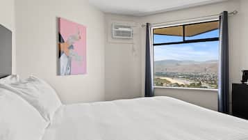 A bedroom with a bed, a window with a view of a landscape, and a wall-mounted air conditioner.