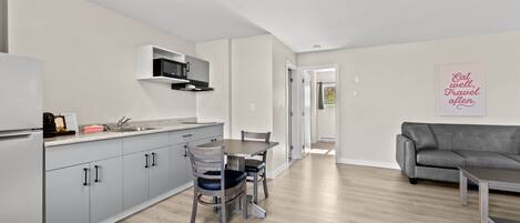 A modern kitchen with grey cabinets, a dining table with chairs, a grey sofa, and a wall with a motivational quote.