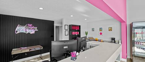 Un espace d’accueil moderne aux couleurs noir et rose, agrémenté d’un néon, d’un comptoir de réception et d’un réfrigérateur contenant des boissons.
