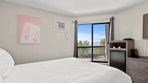 A bedroom with a bed, a small refrigerator, a desk, and a window with a view of the outdoors. - The Vista Inn (Kamloops)