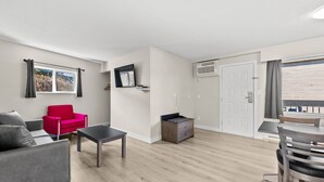 A modern living room with a grey sofa, a red chair, a wooden dining table, and a grey coffee table. - The Vista Inn (Kamloops)
