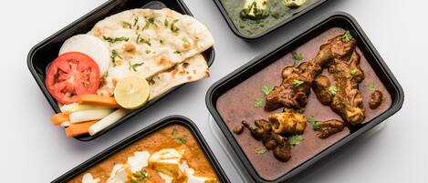 Variedad de platos de la cocina india en recipientes negros, incluyendo curries de paneer, pollo y verduras, acompañados de pan naan y arroz.