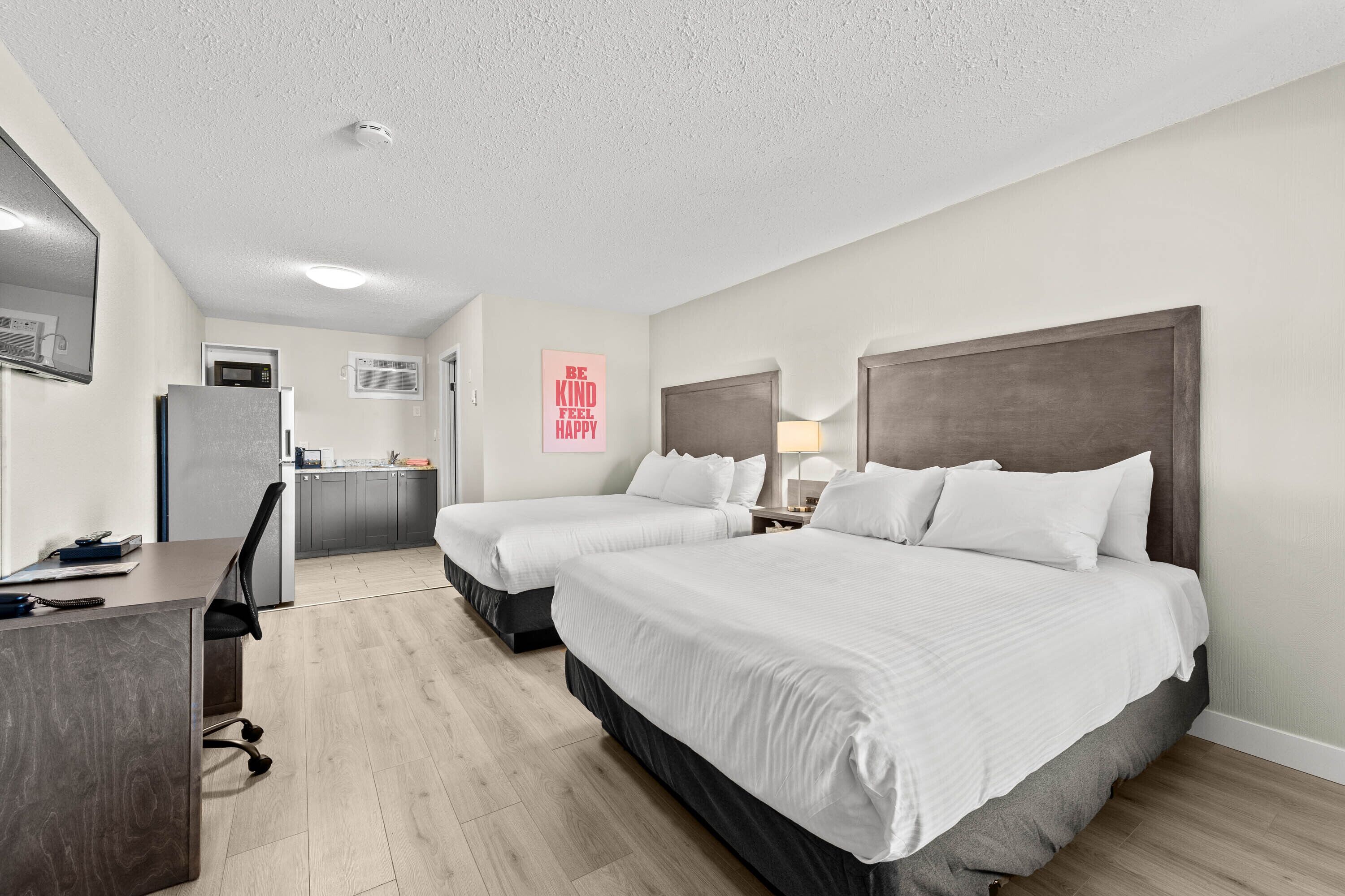 A hotel room with two beds, a desk, a chair, a microwave, and a small kitchenette.