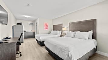A hotel room with two beds, a desk, a chair, a microwave, and a small kitchenette.