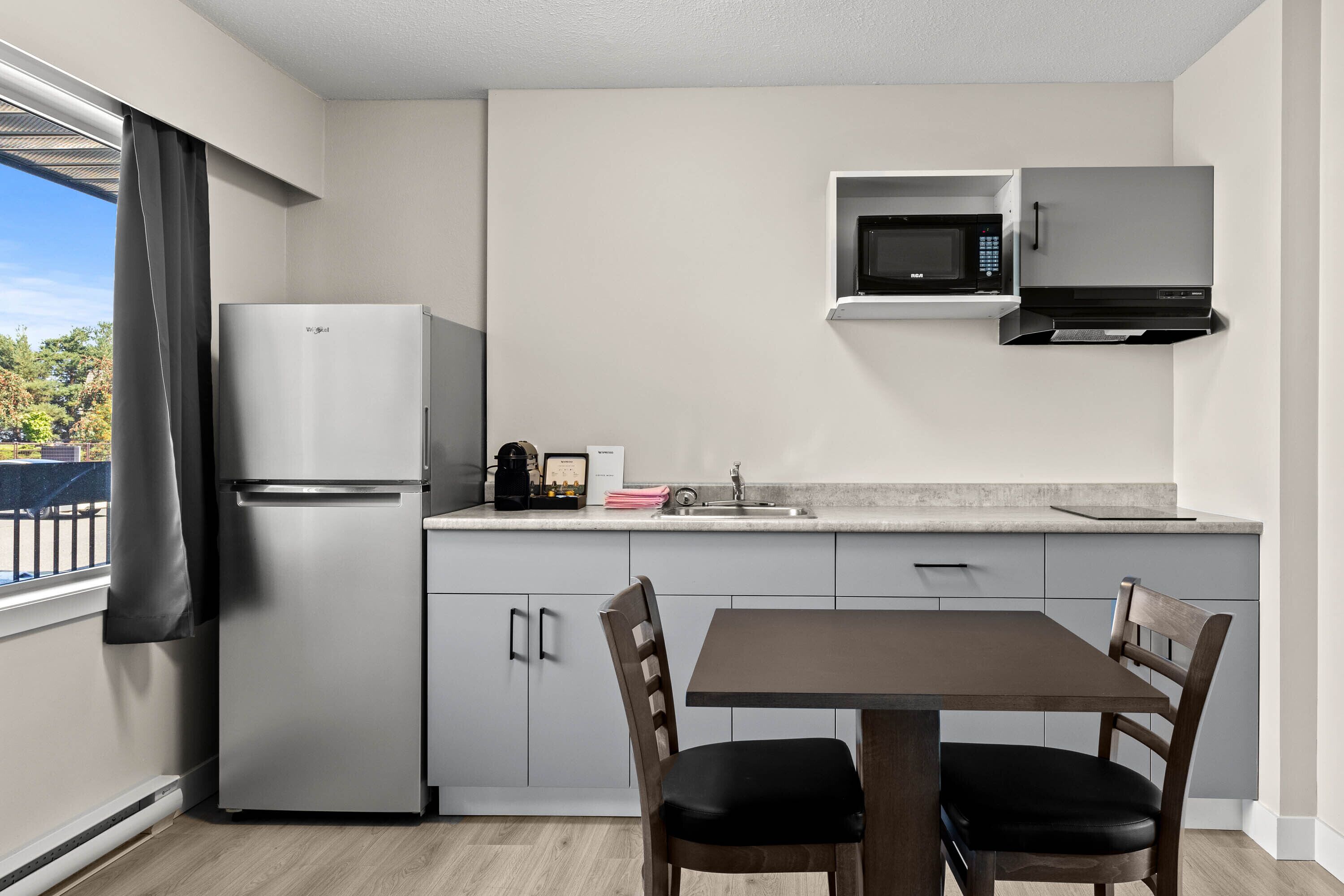 A modern kitchen with a built-in refrigerator, microwave, and sink. There is a dining table with two chairs.
