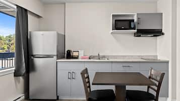 A modern kitchen with a built-in refrigerator, microwave, and sink. There is a dining table with two chairs.