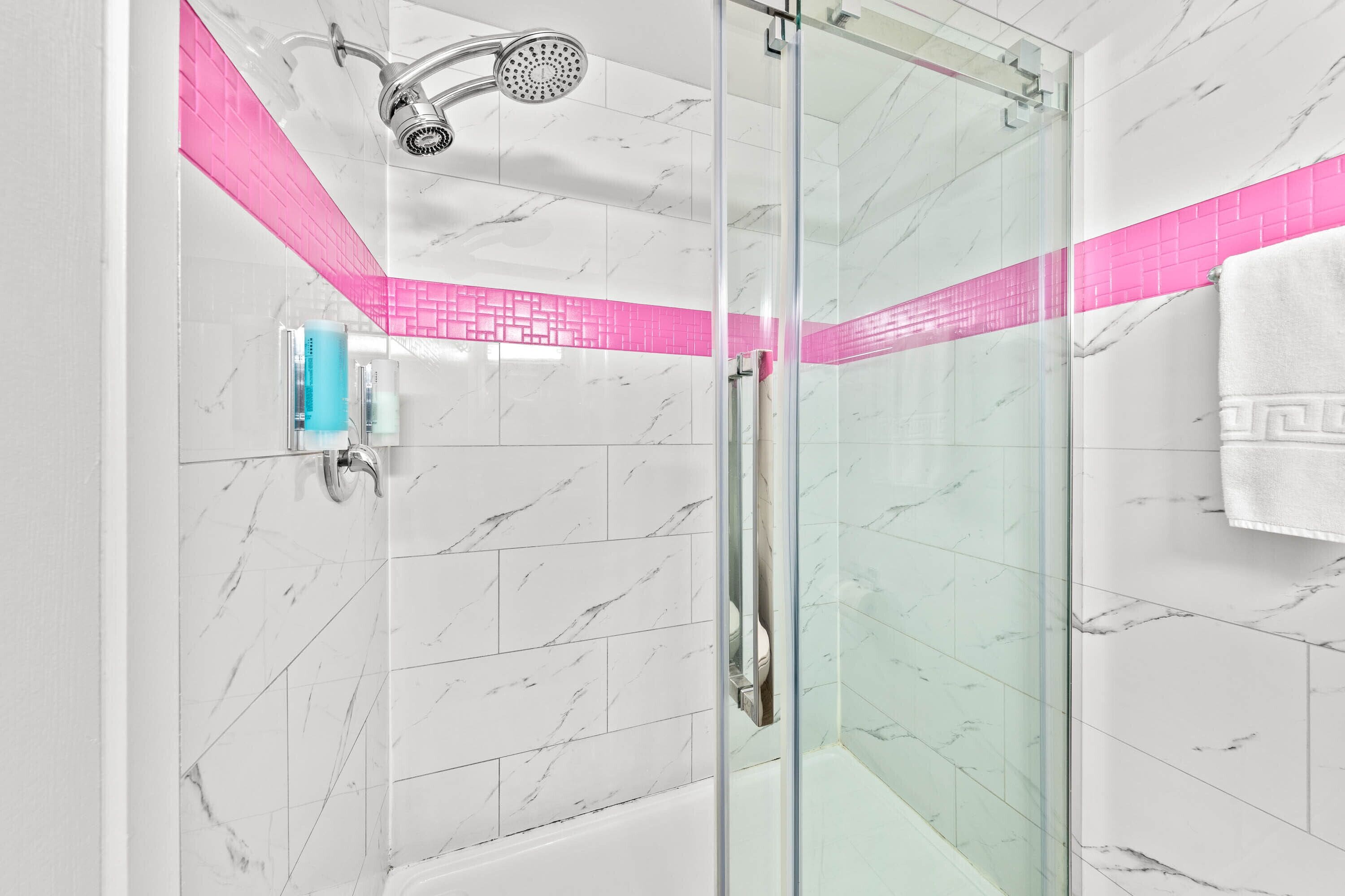 A modern shower with a glass door, a handheld showerhead, and a pink-tiled accent wall.