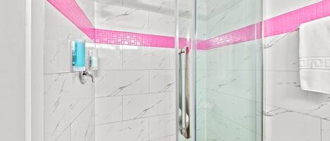 A modern shower with a glass door, a handheld showerhead, and a pink-tiled accent wall.