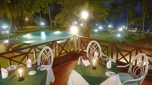 Comedor con mesas dispuestas para dos, con vistas a una piscina y palmeras.
