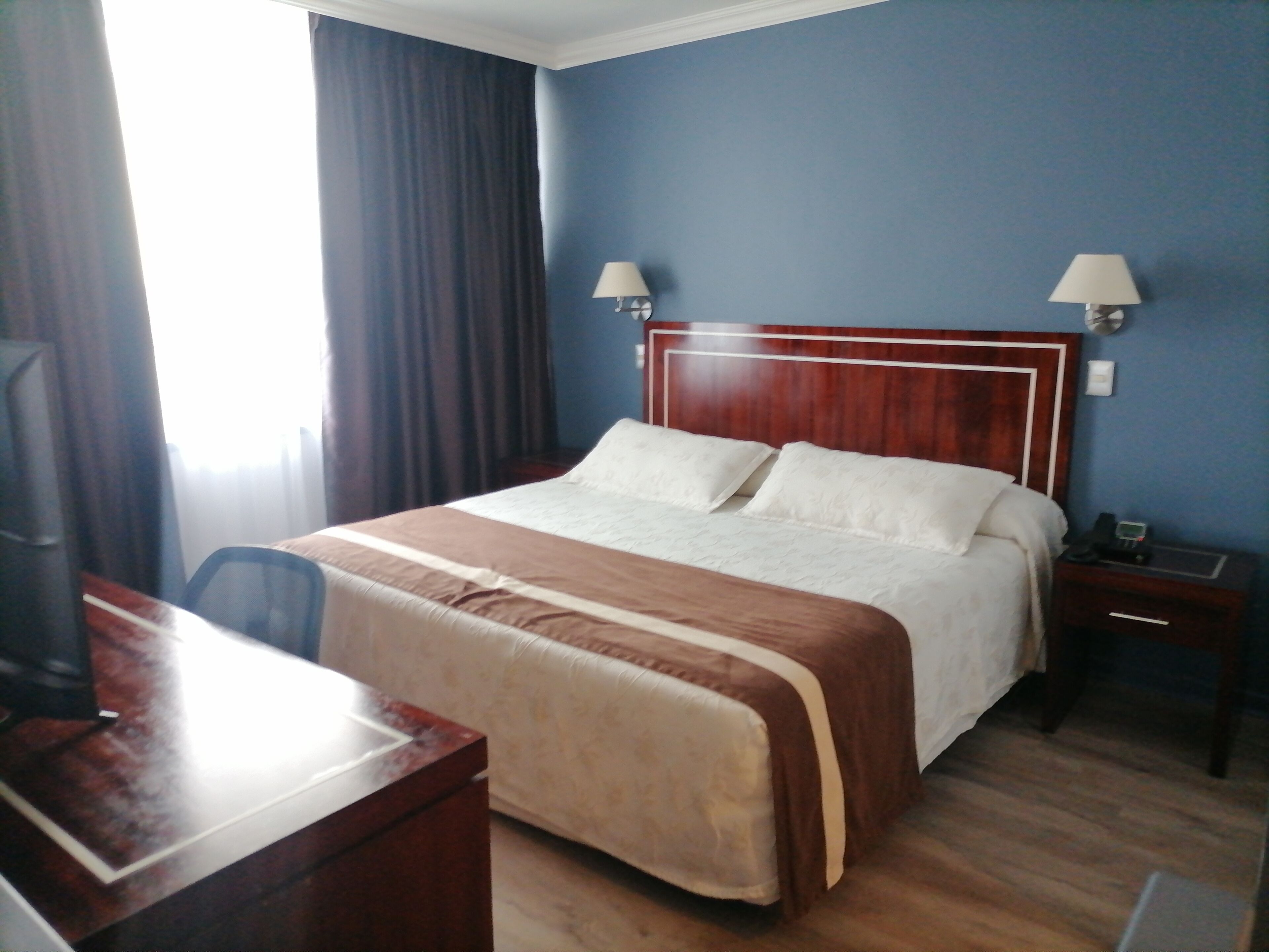 A hotel room with a large bed, two bedside lamps, a desk, and a chair.