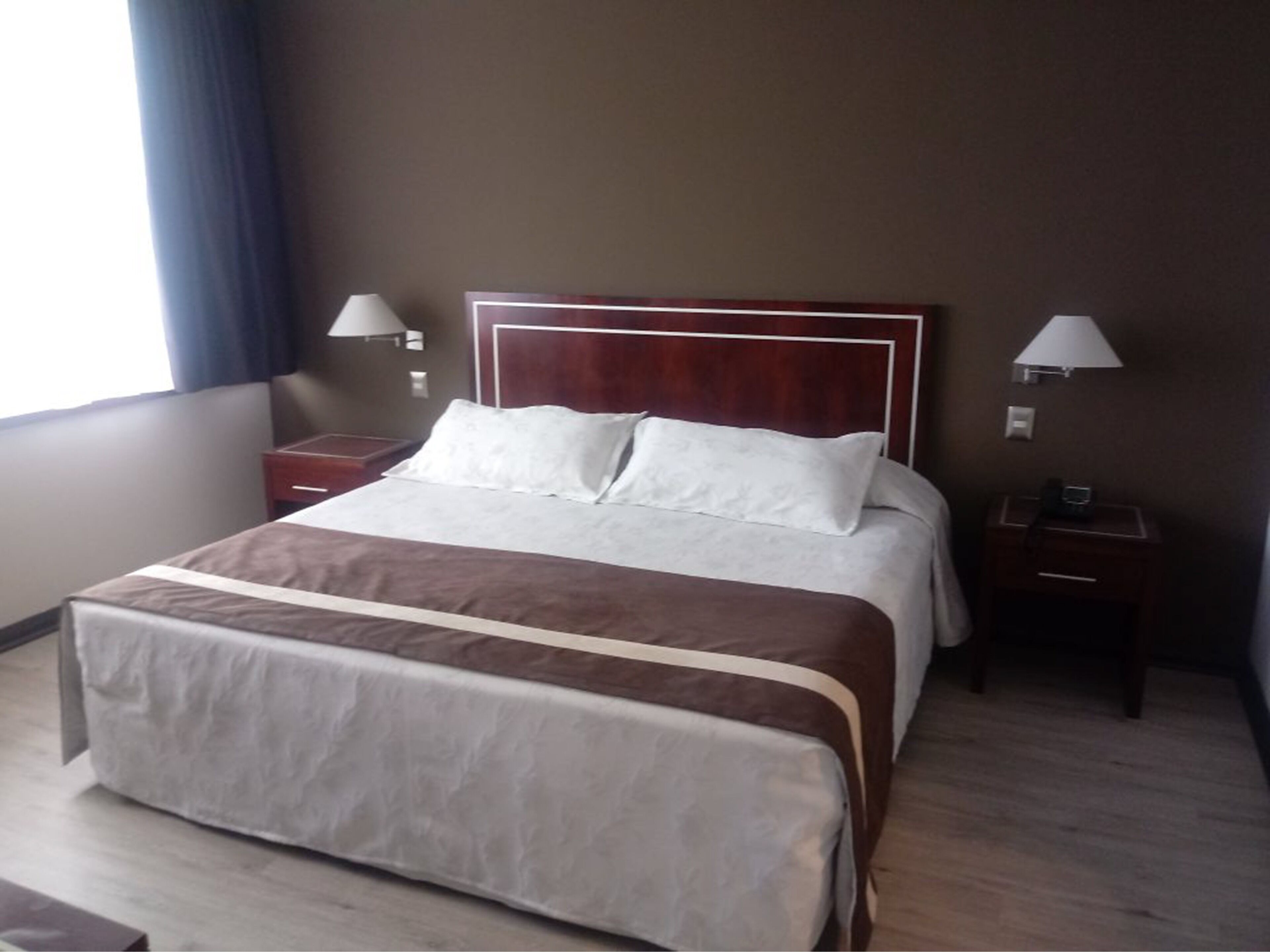 A hotel room with a large bed, two bedside tables, and two wall-mounted lamps.