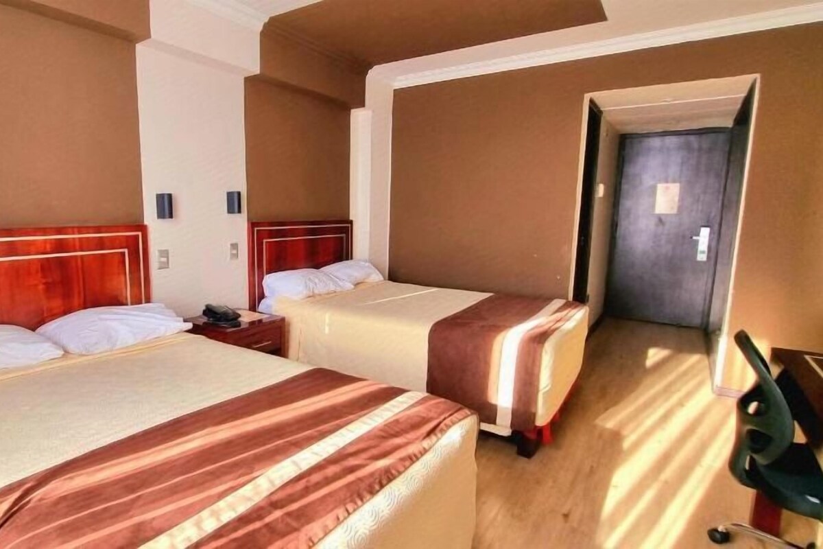 A hotel room with two beds, a wooden headboard, a nightstand, and a door leading to another room.