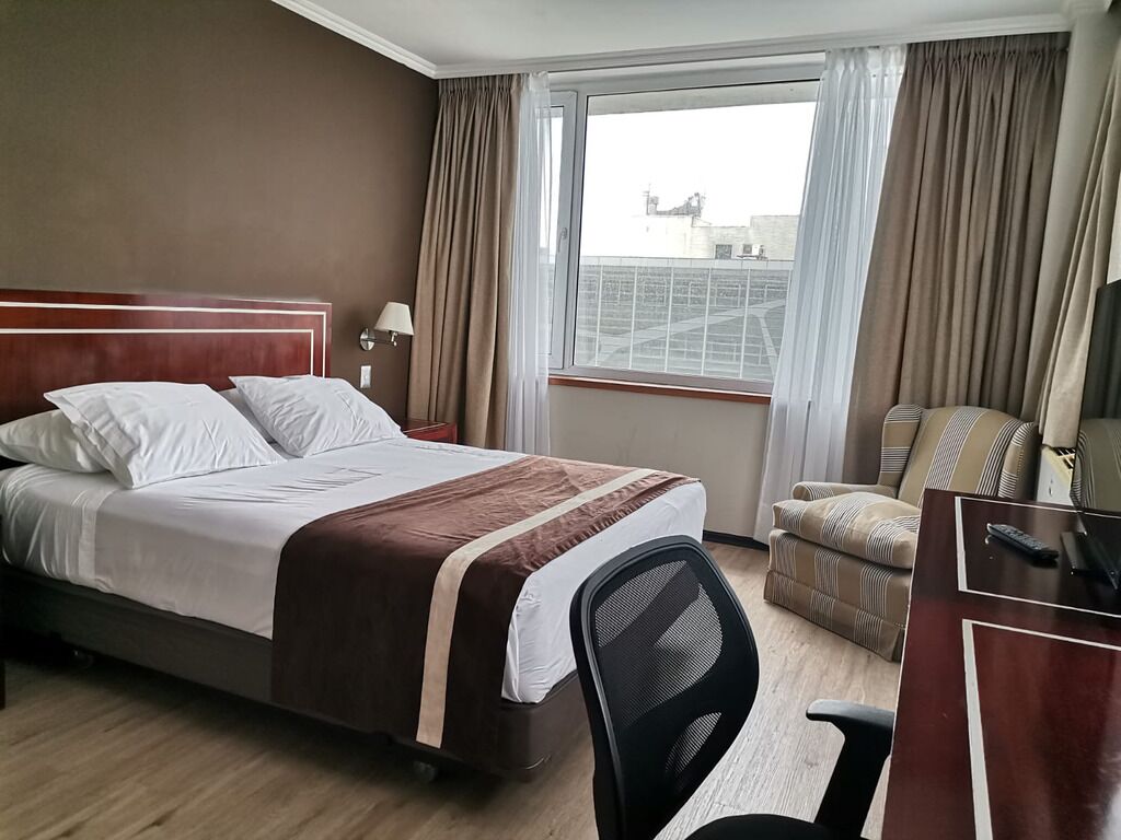 Une chambre d’hôtel avec un lit, un bureau, une chaise et une fenêtre avec des rideaux.