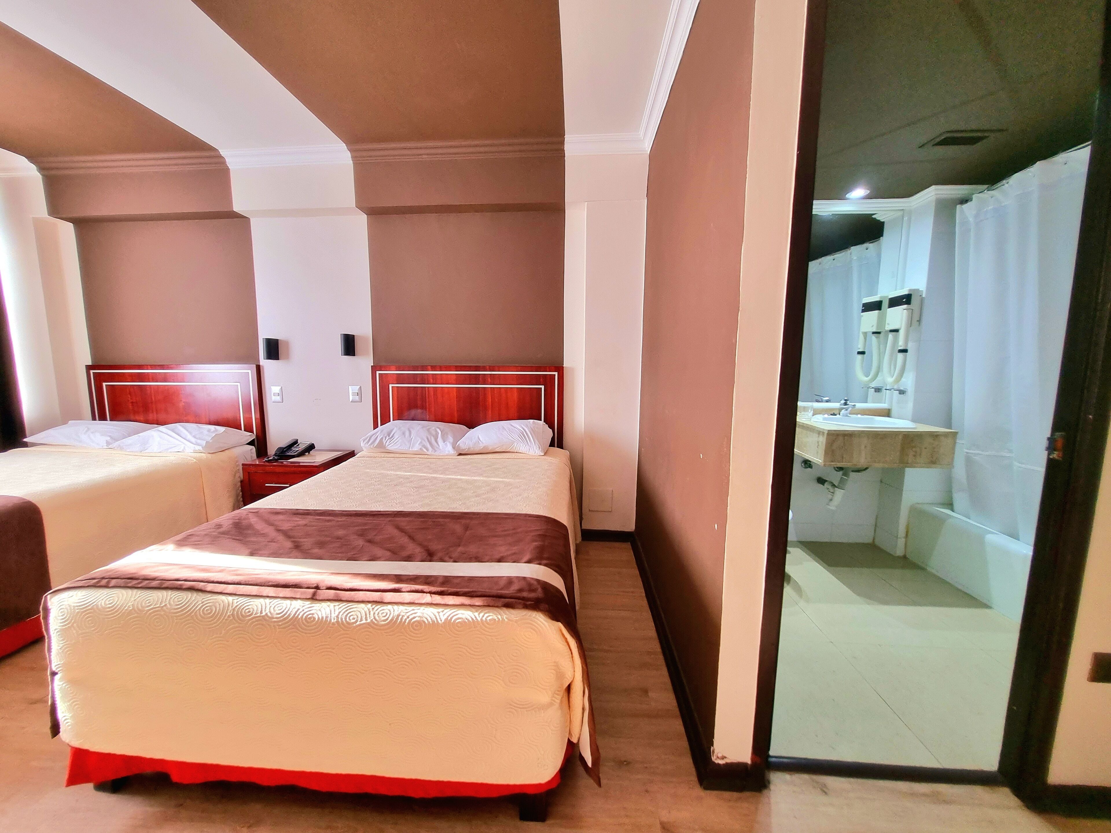 A hotel room with two beds, a bathroom with a sink and mirror, and a door leading to another room.