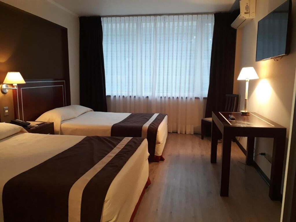 Une chambre d’hôtel avec deux lits, un bureau, une chaise, une télévision et une fenêtre avec des rideaux.