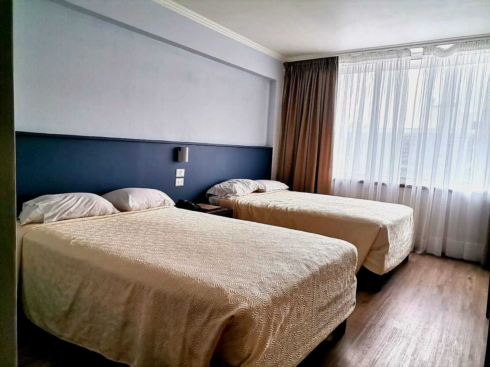 Une chambre d’hôtel avec deux lits, un mur d’accent bleu, une fenêtre avec des rideaux et une table de chevet avec une lampe.