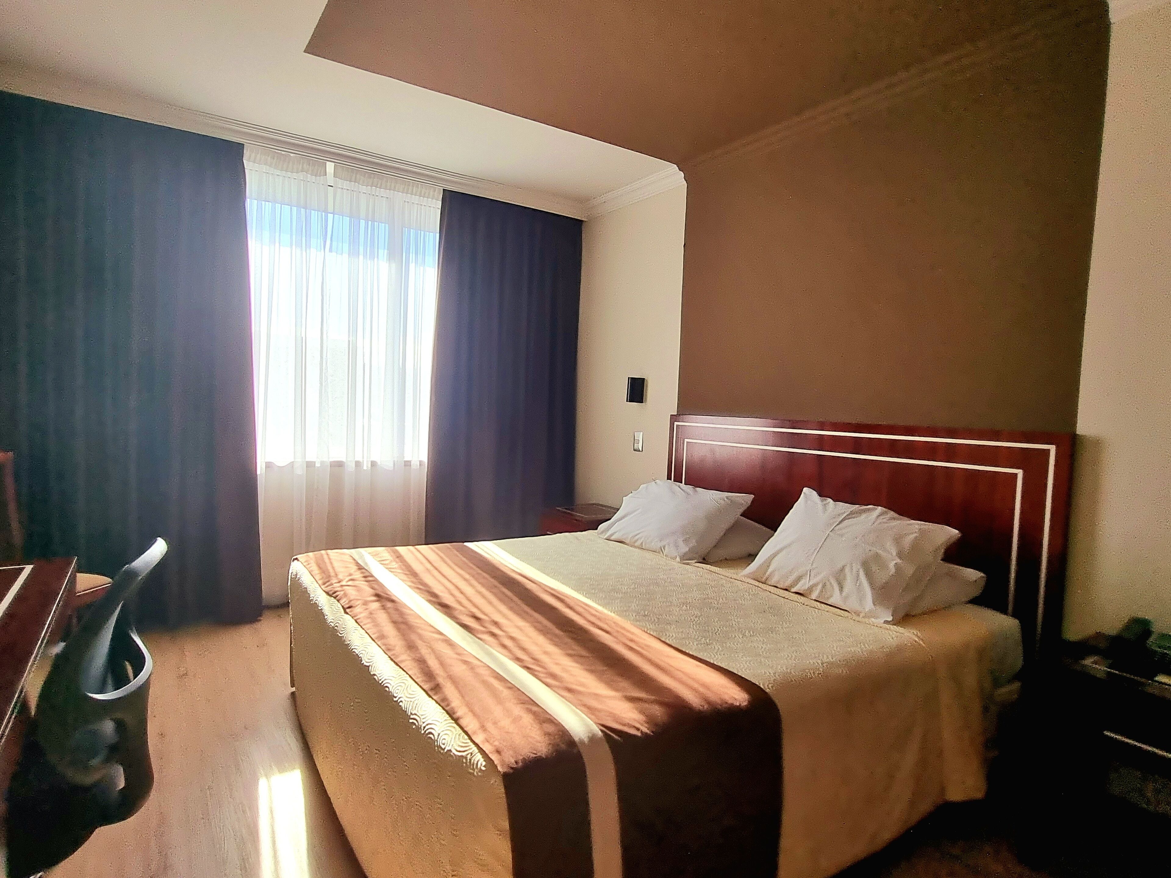 A hotel room with a bed, a desk, and a window with curtains.