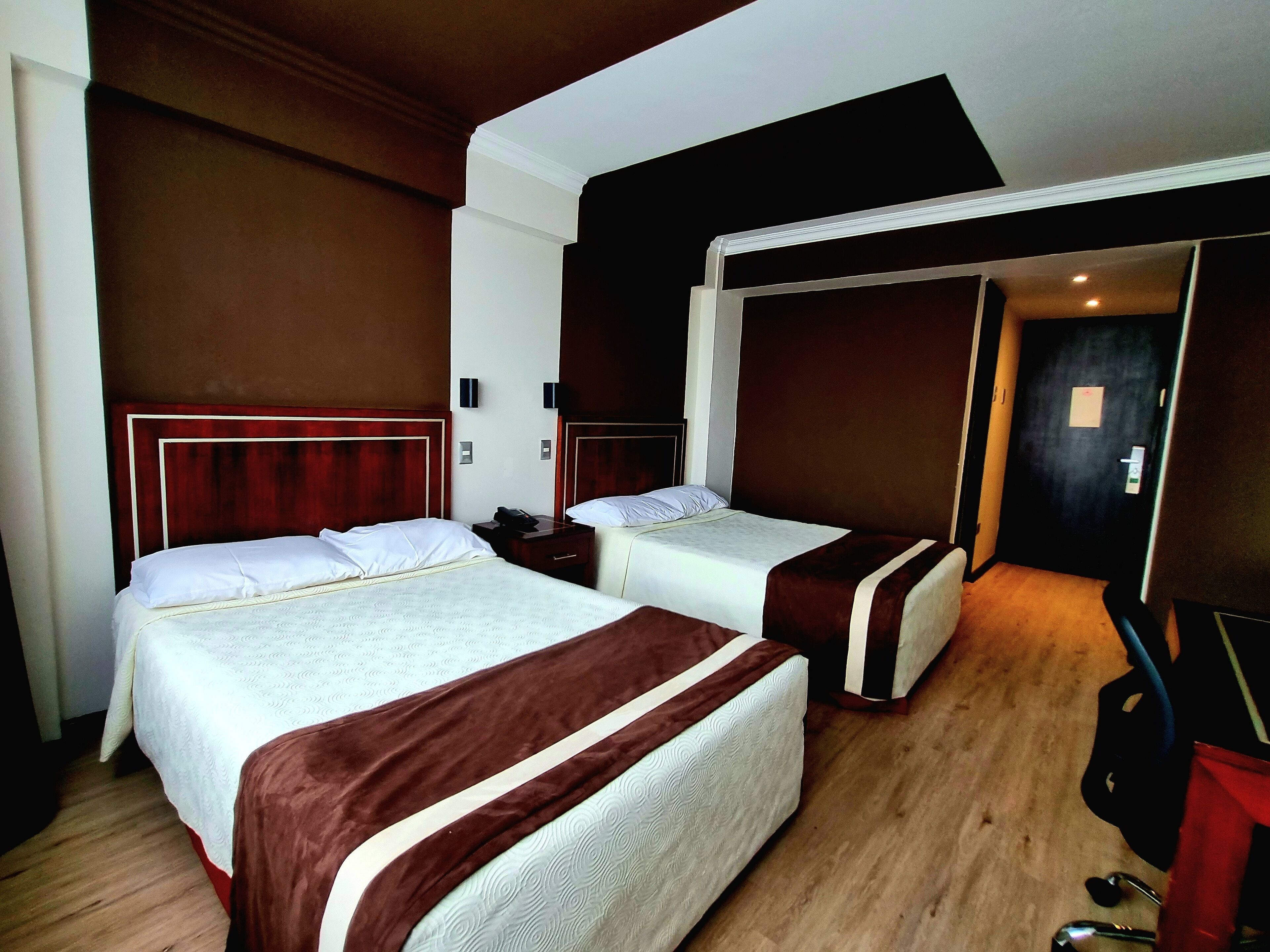 Una habitación de hotel con dos camas, cabeceros de madera, un escritorio y una televisión.