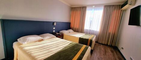Une chambre d’hôtel avec deux lits, un téléviseur à écran plat, une table de chevet avec une lampe et une fenêtre avec des rideaux.