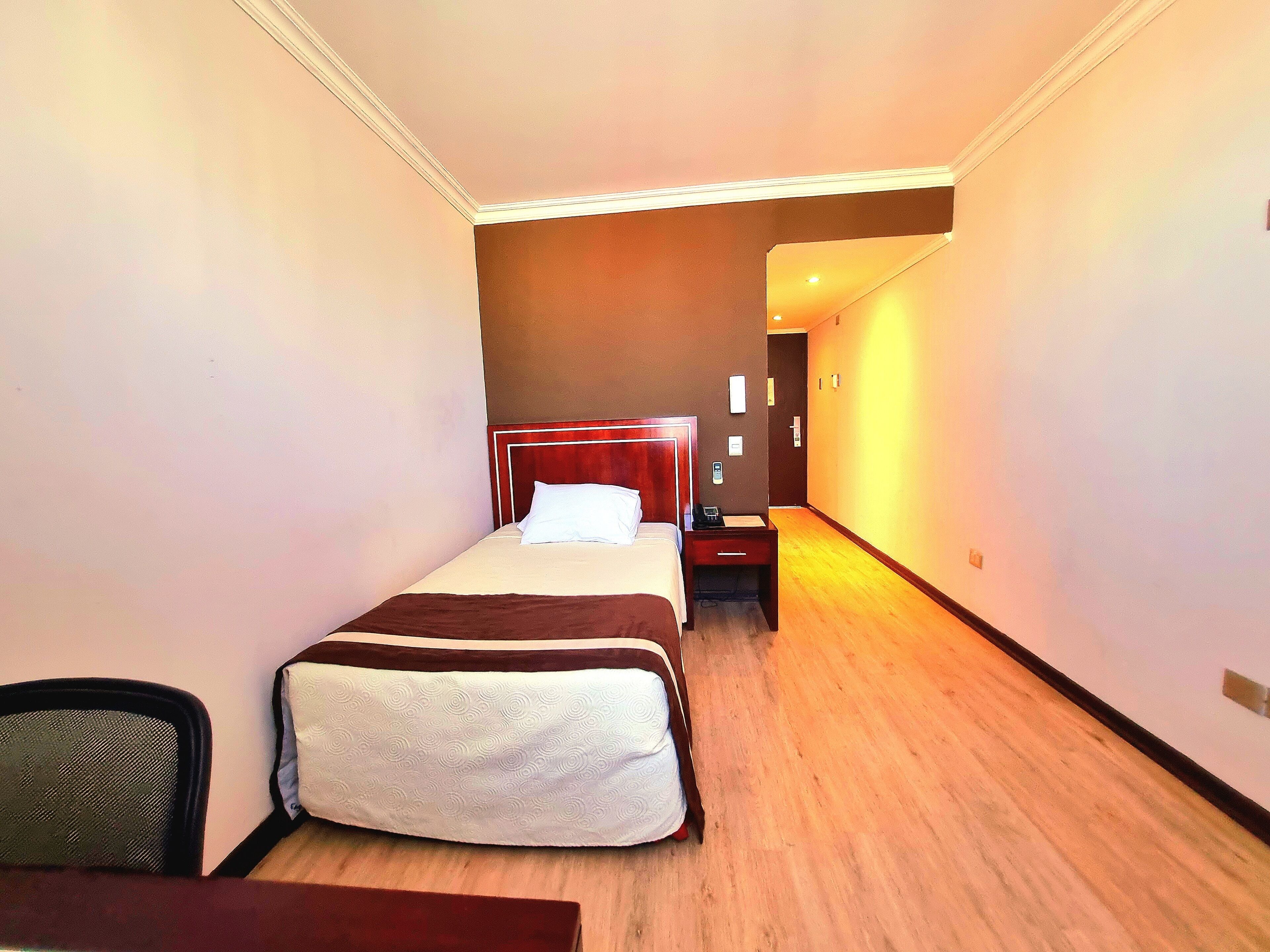 Habitación de hotel con una cama individual, mesita de noche y una silla.