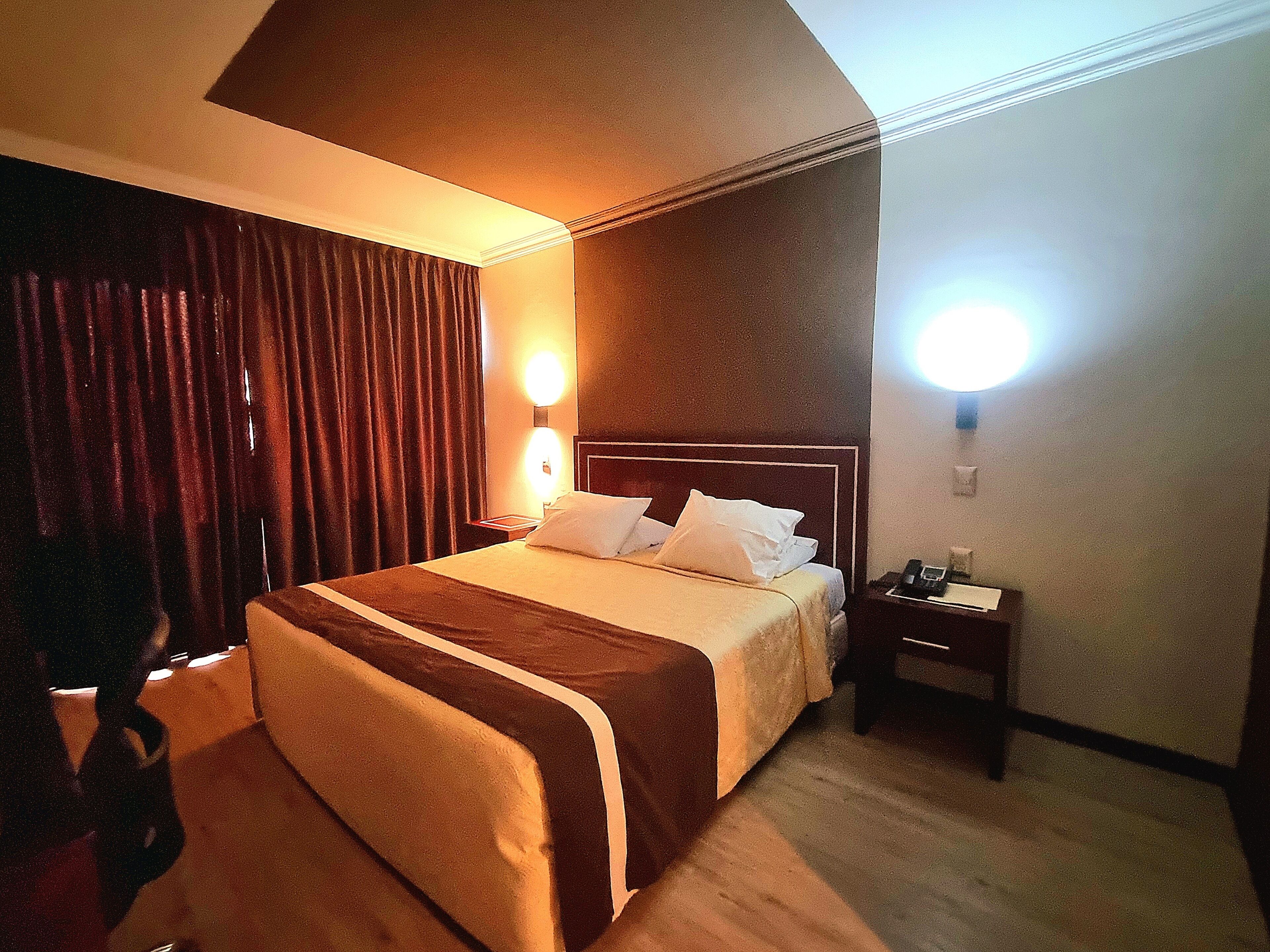 Una camera d'albergo con un letto grande, un comodino, una lampada e una tenda.