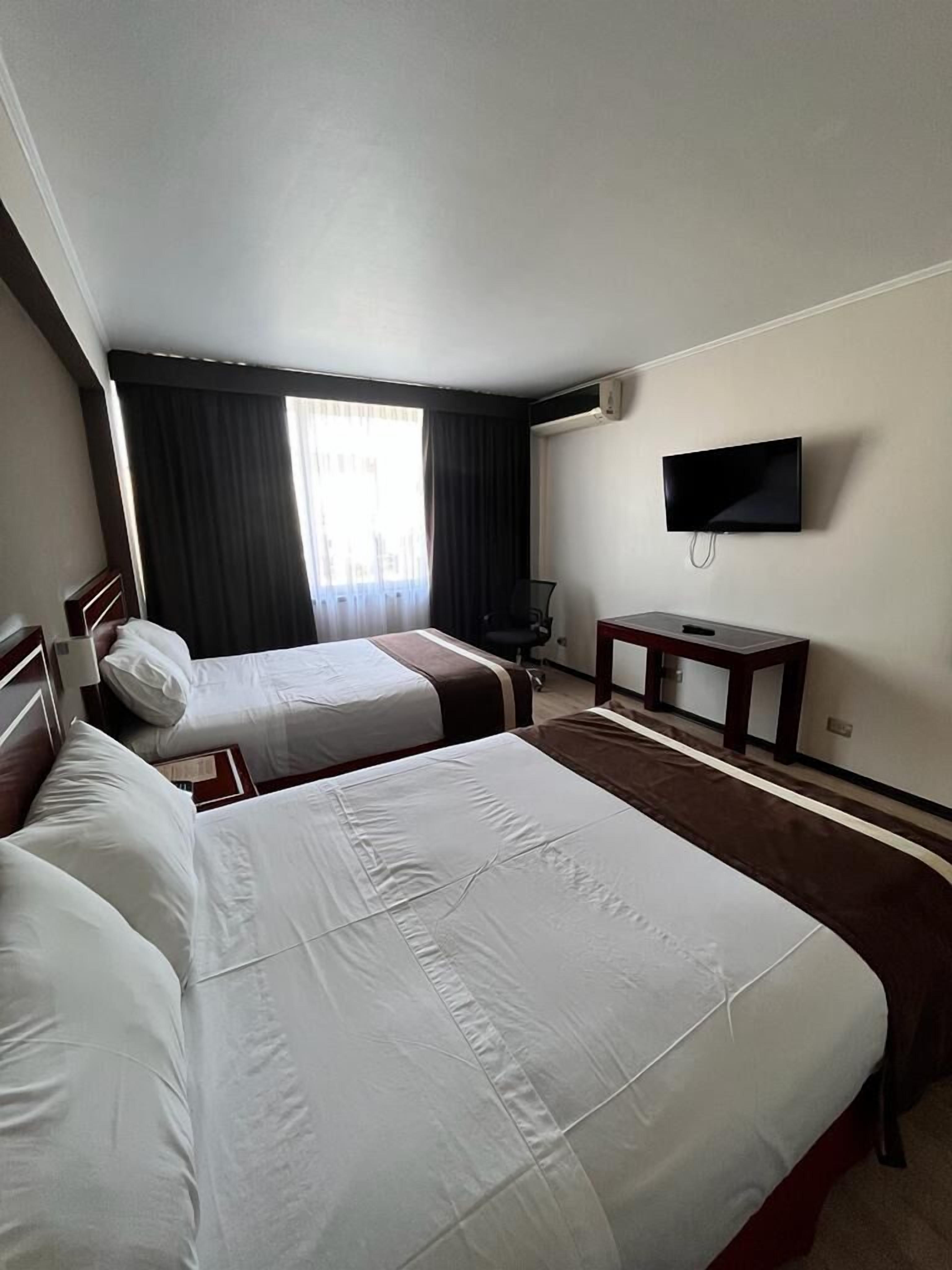 A hotel room with two beds, a TV, a desk, and a chair.