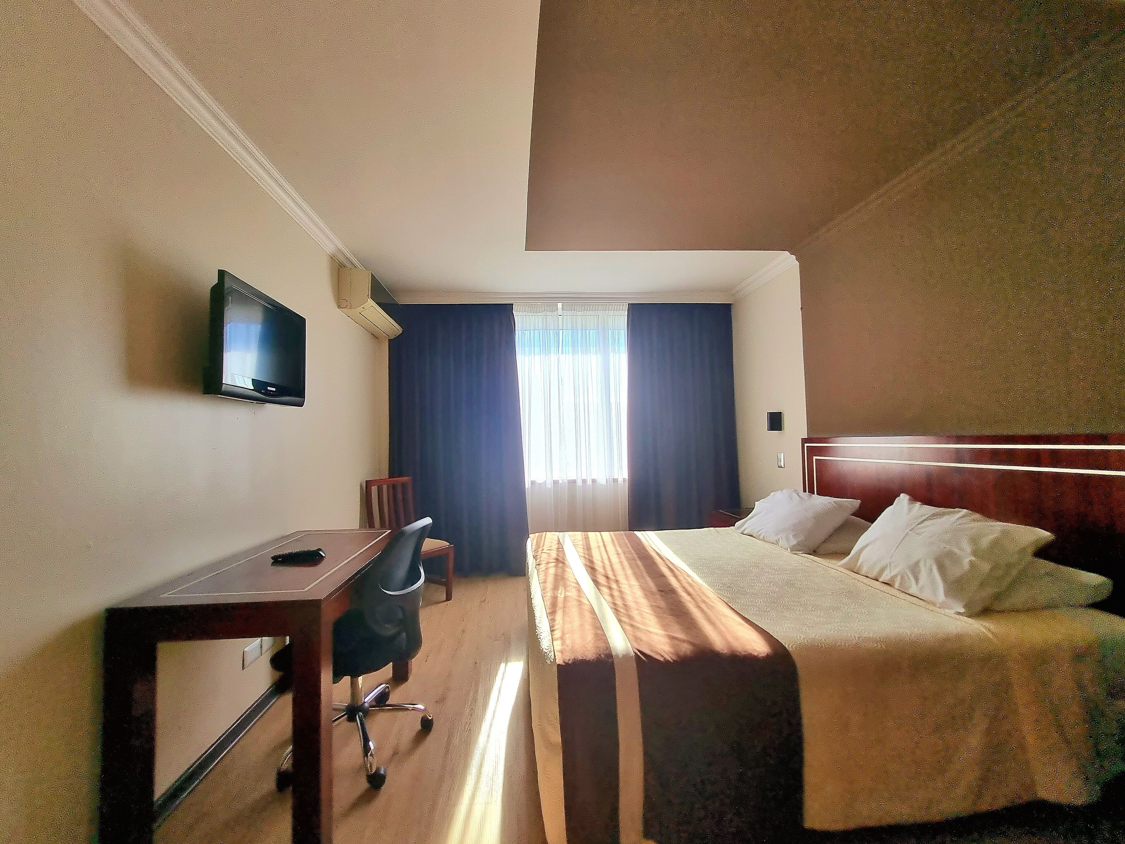 A hotel room with a bed, a desk, a chair, a television, and a window with curtains.