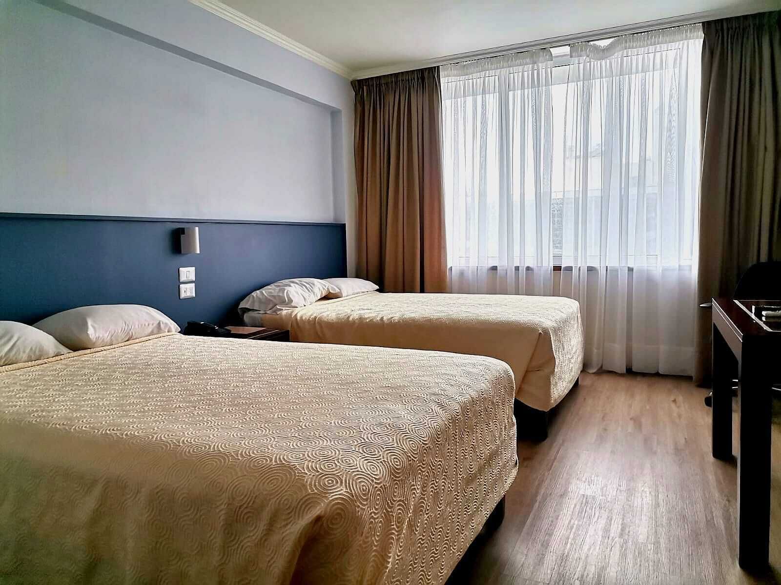 Habitación de hotel con dos camas, un escritorio y una ventana con cortinas.