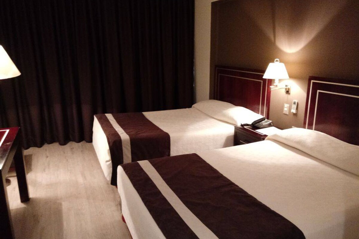 A hotel room with two beds, a desk, a lamp, and a telephone.