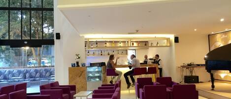 A modern lobby with a bar area, seating, and a piano.