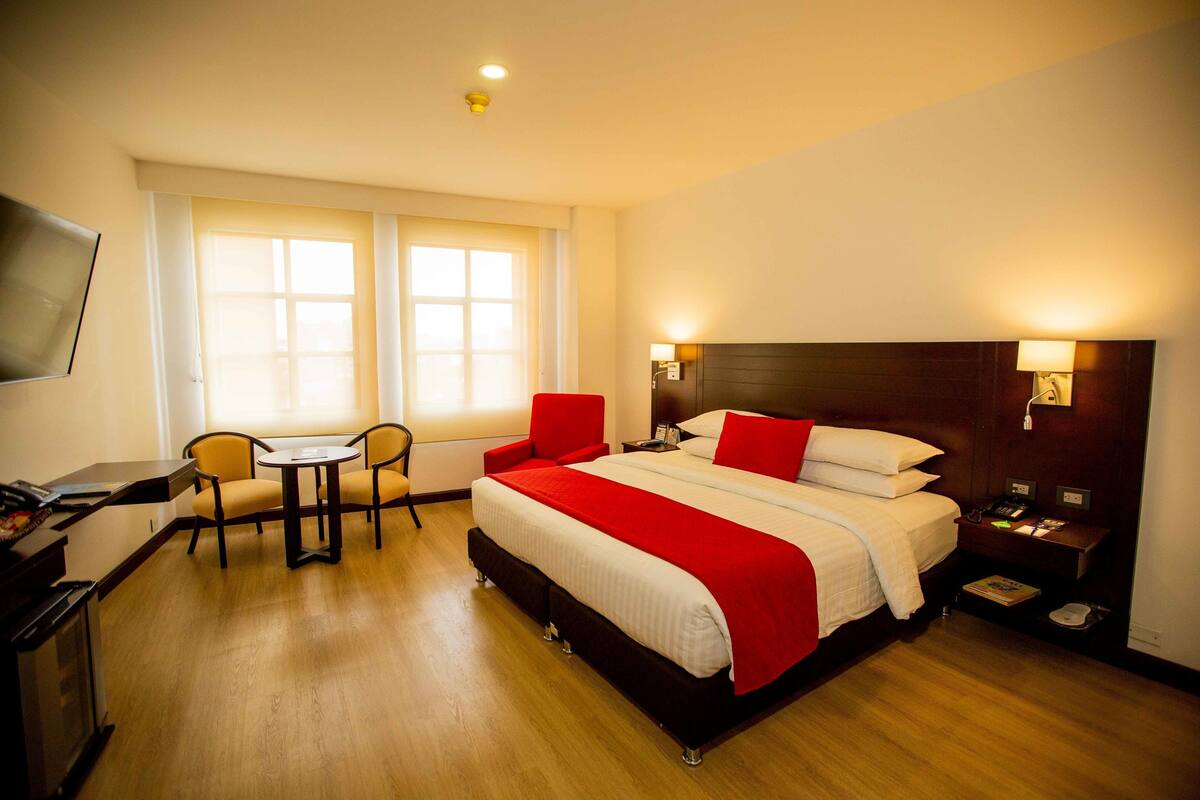 Una habitación de hotel con cama, mesita de noche, lámpara, escritorio, silla y televisor.