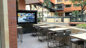 Outdoor dining area with tables and chairs, a flat-screen TV, and a view of the surrounding street.